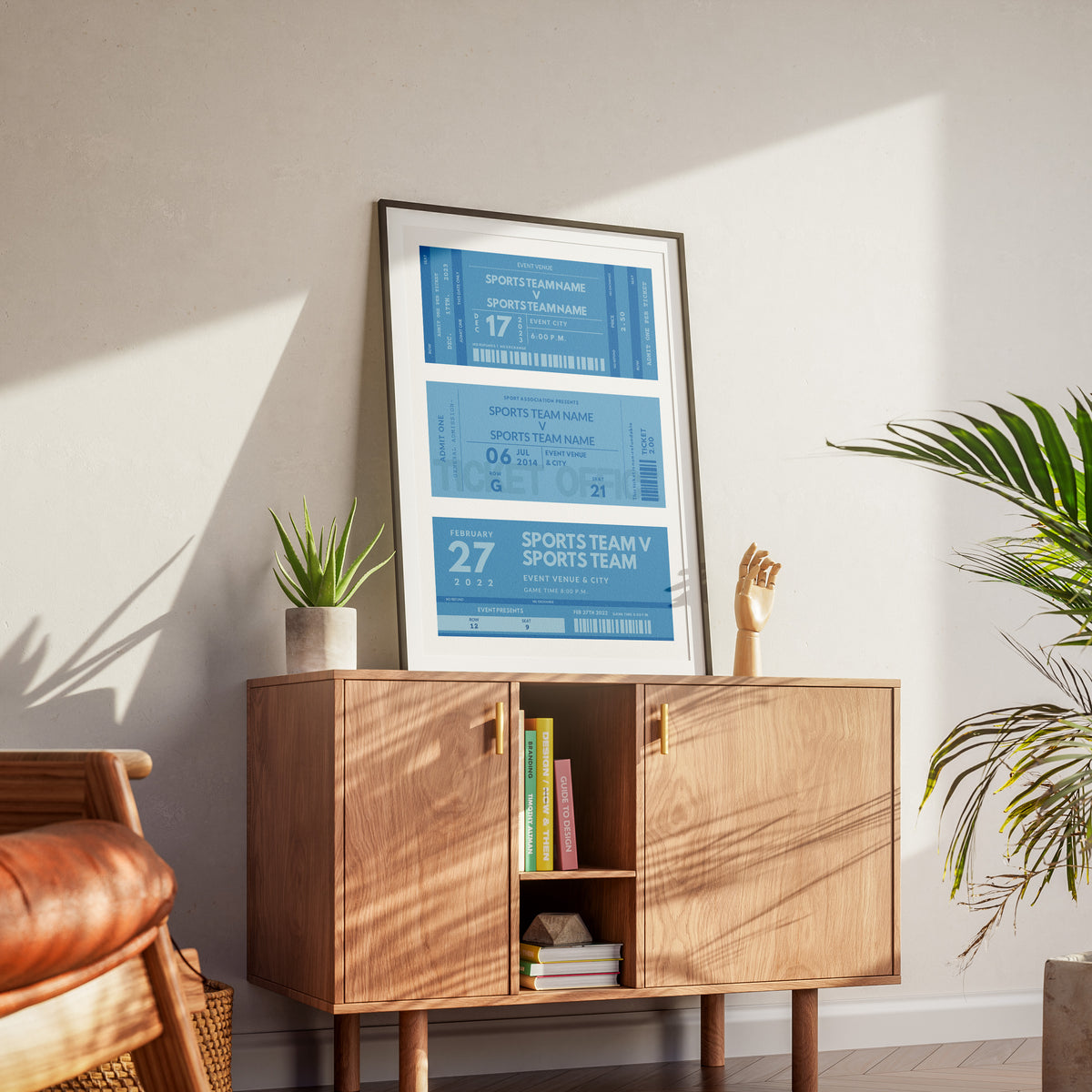 Personalized vintage athletic venue print, with three blue sporting event tickets on it. The art is in a black frame on a wood cabinet in a livingroom.