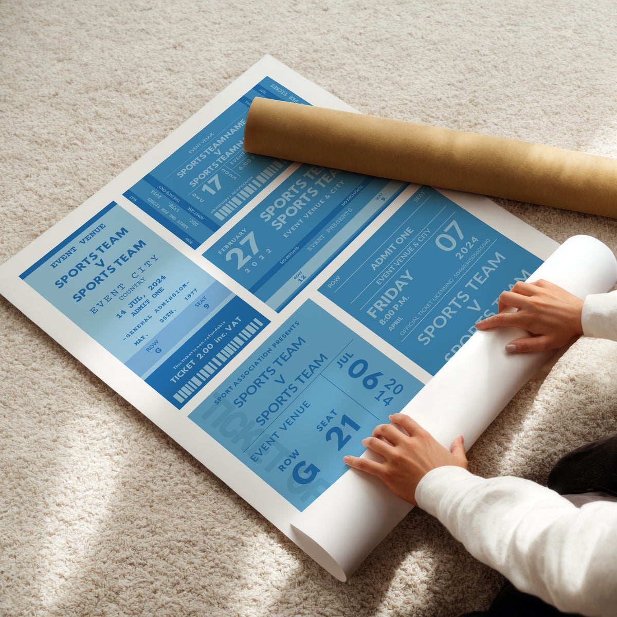 A person unrolls a large sports ticket wall poster on a beige carpet, with a brown cardboard mailing tube placed on top. The poster features multiple blue and white ticket designs with text such as 'SPORTS TEAM', 'EVENT VENUE', and dates. This is where custom details will be added.