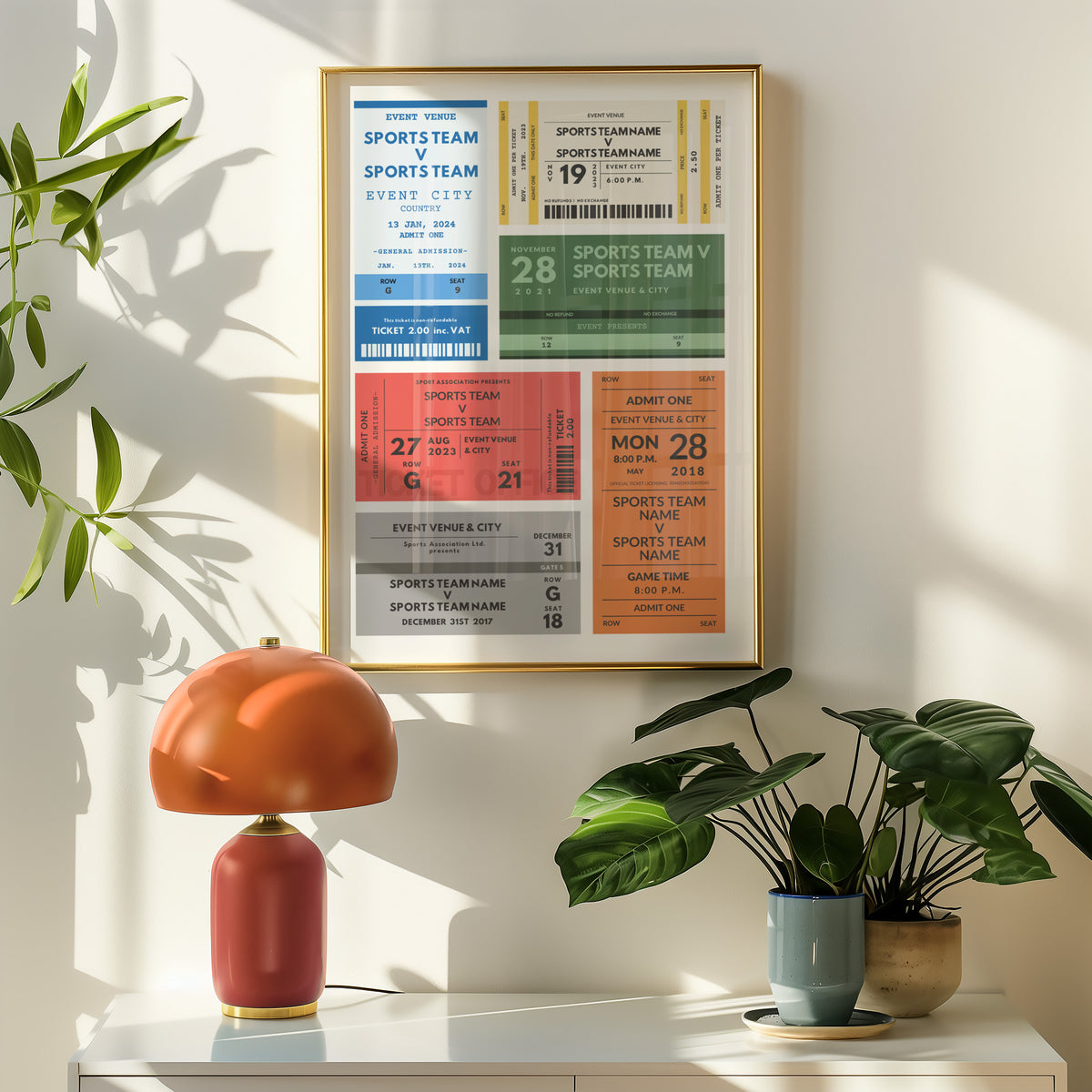 A framed wall art print featuring personalised sports event tickets in blue, green, orange, and cream tones, hung on a warm beige wall above a white console table. The scene includes a terracotta table lamp, potted green plants, and soft natural shadows.