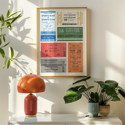 A framed wall art print featuring personalised sports event tickets in blue, green, orange, and cream tones, hung on a warm beige wall above a white console table. The scene includes a terracotta table lamp, potted green plants, and soft natural shadows.
