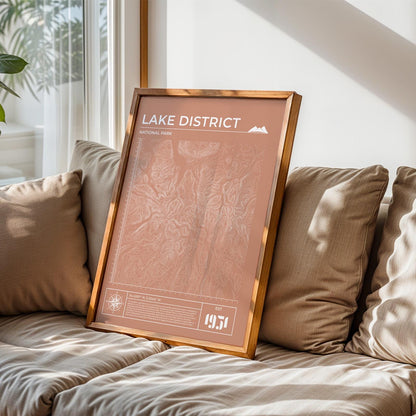 Framed Lake District map art poster in terracotta on sofa, perfect gift for hikers and outdoor adventure lovers.