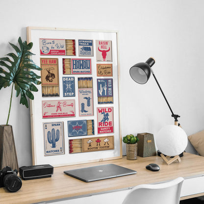 A framed printable home decor piece showcasing vintage matchbook designs with a Wild West theme. The artwork is displayed on a wooden desk with a lamp and laptop.