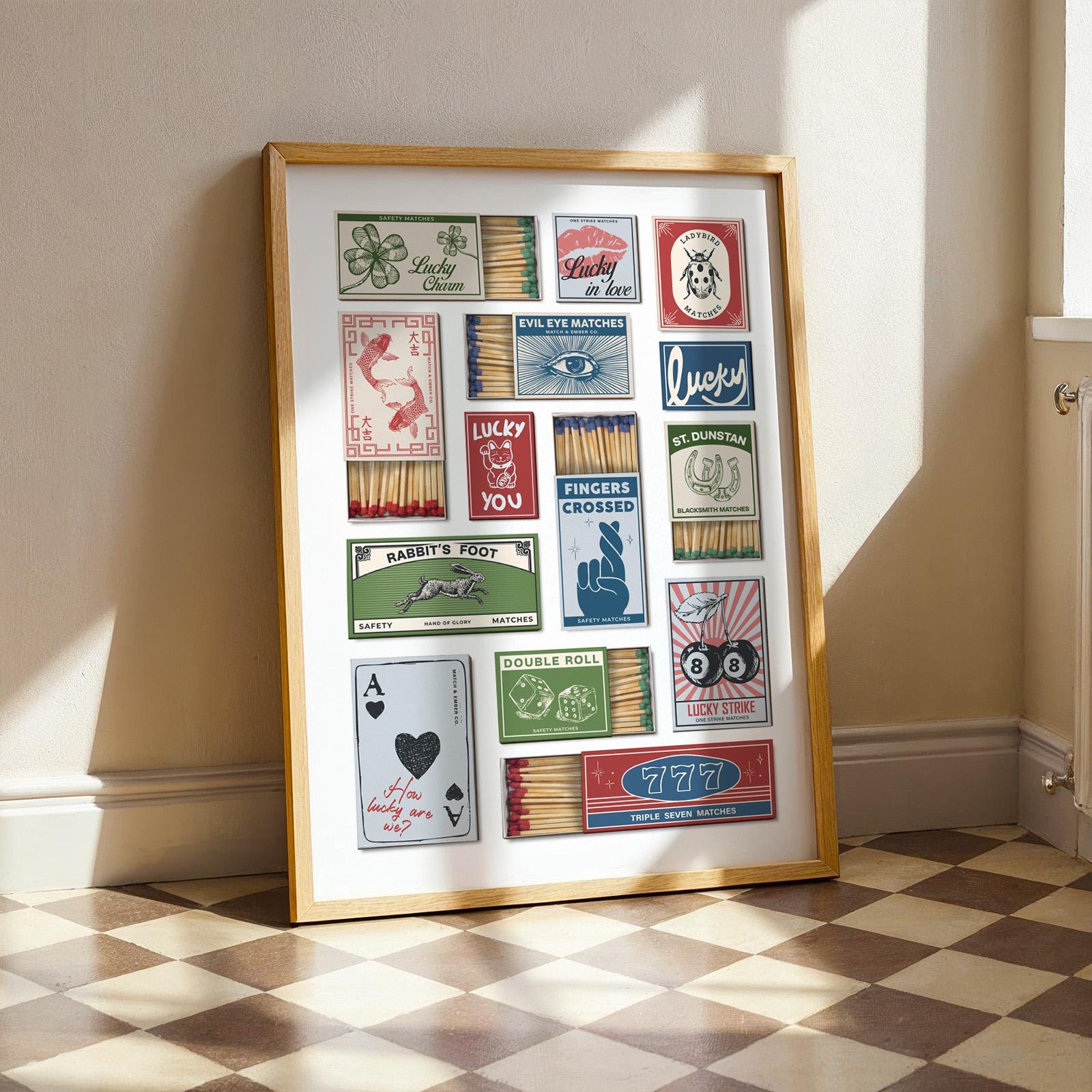 A framed print displaying a collection of matchbox designs with lucky symbols. The designs include a four-leaf clover, koi carp, an eye, a rabbit's foot, and playing cards. The print is in a wooden frame and is set against a white backdrop.