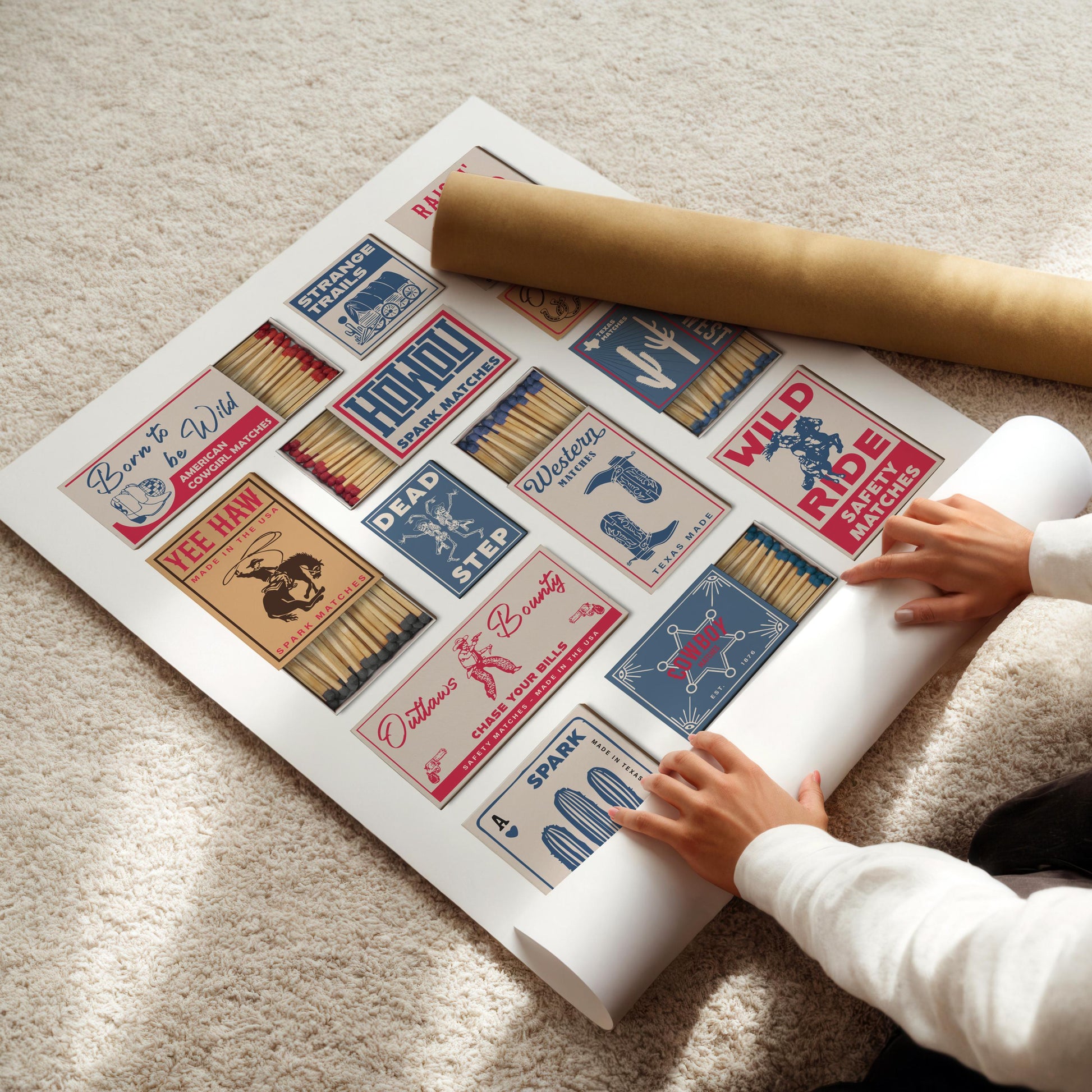 A white poster with retro matchbox designs, featuring Western-themed graphics and text. The poster is being unrolled on a light-coloured carpet, with a rolled-up poster tube in the background. The matchbox designs include phrases like "Yee Haw".