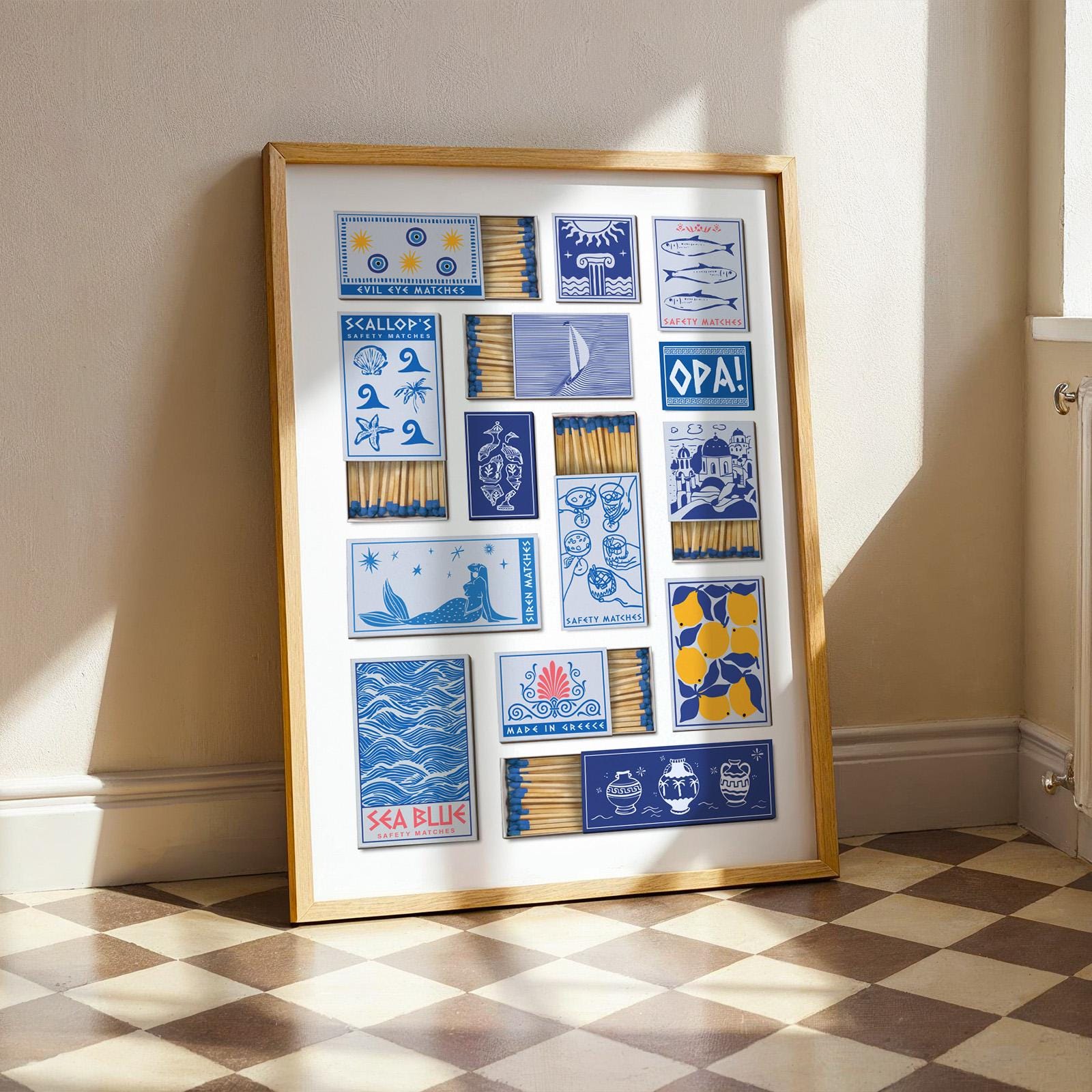 A framed greece matchbook print easy to download displaying a collection of matchbox designs with blue and yellow illustrations. The designs include nautical themes and the text "SEA BLUE". The frame is a light wood colour.