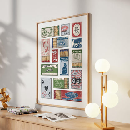 An eclectic style print showcasing vintage matchbox designs with illustrations and text such as "Rabbit's Foot". The artwork is displayed on a light-coloured wall, with a wooden frame. A modern lamp with spherical lights is on the right.