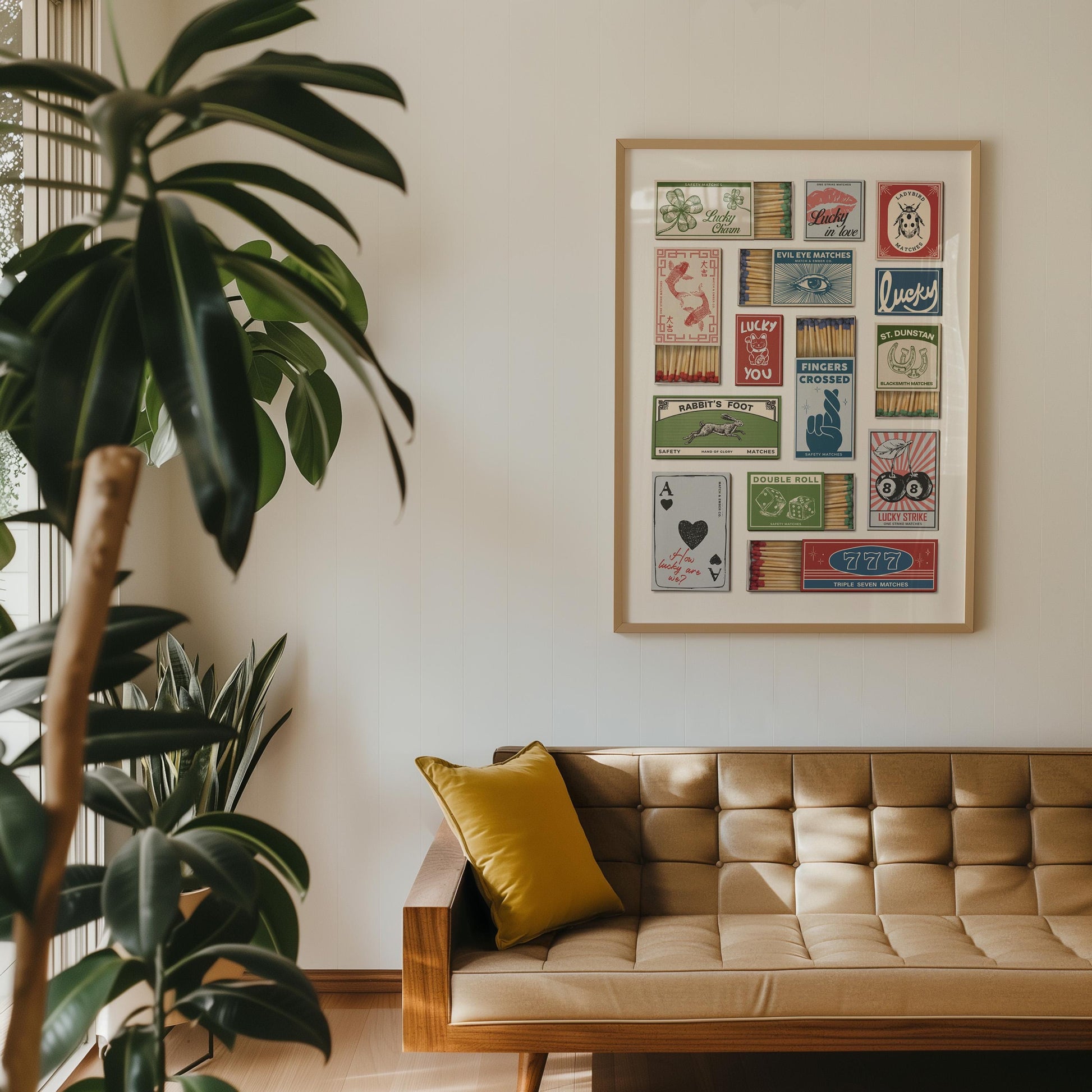 A home decor item displaying a collage of vintage matchbox designs with diverse graphics and text, such as "Lucky". The artwork hangs on a white wall above a mid-century sofa with a yellow cushion.