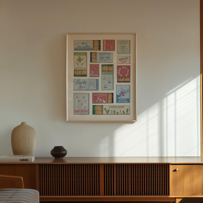 A stylish poster displaying vintage matchbox designs with ski-themed graphics and text. The artwork features various colours and text such as "Après Ski Club", "Ski Run", and "Carve Hard". The print is on a white wall above a wooden cabinet.
