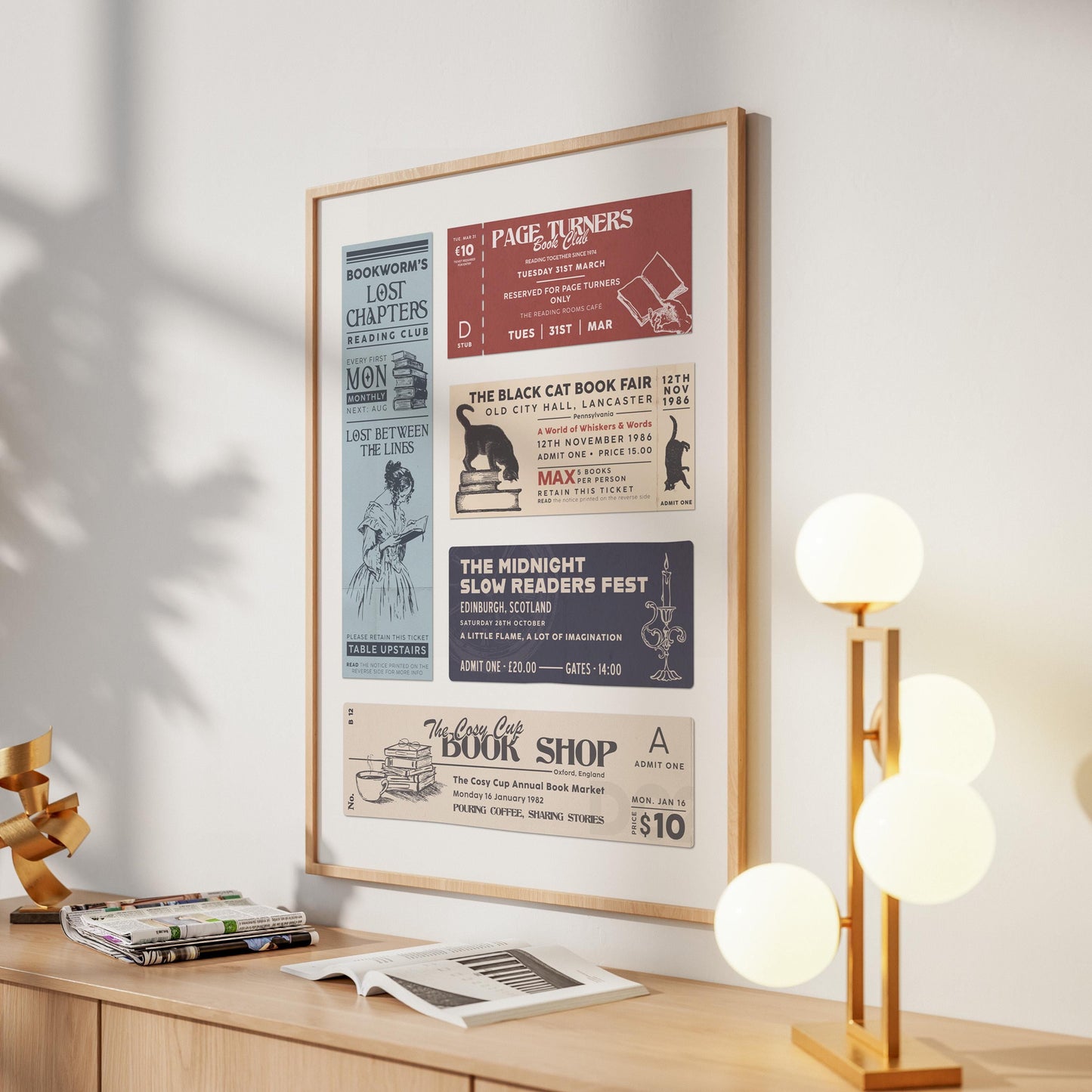 A book lovers art gift with vintage book club and book fair tickets, hung on a wall. A stack of books and a modern lamp are in front of the print.