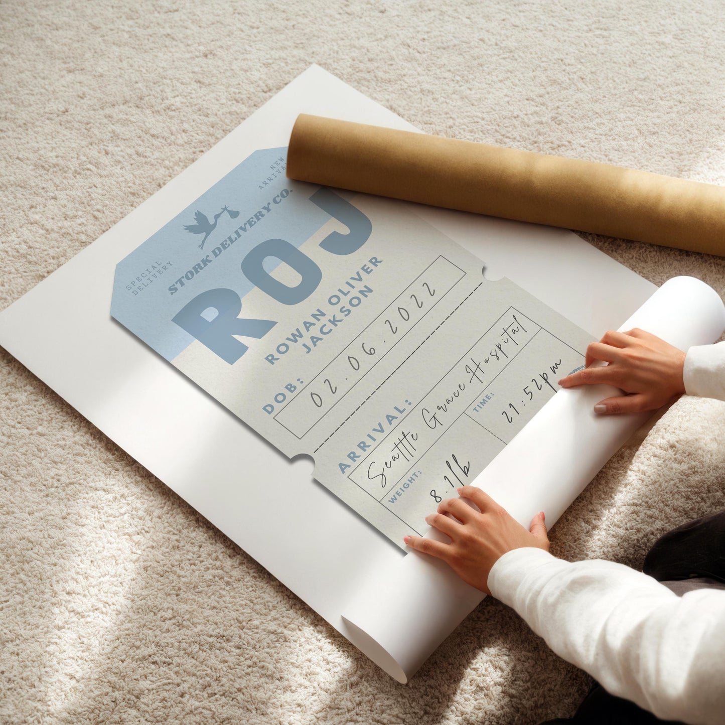 A baby blue wall art piece being rolled out on the floor. The art has a airplane boarding pass sle but with newborn statistics on it such as arrival time and hospital. The initials are used to make the airport code.