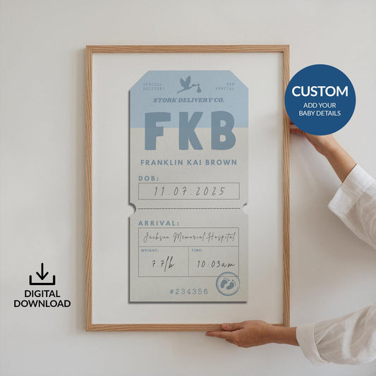Someone holding up a framed poster against a white wall. The art is a blue vintage luggage tag design with baby arrival details on it such as name, weight and time of birth.