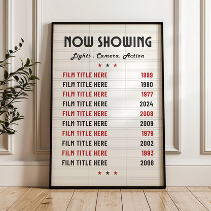 A white panelled wall background with a print in a black frame leaning on the wall. The print is a marquee movie theatre board style with bespoke film choices and their release dates on it.