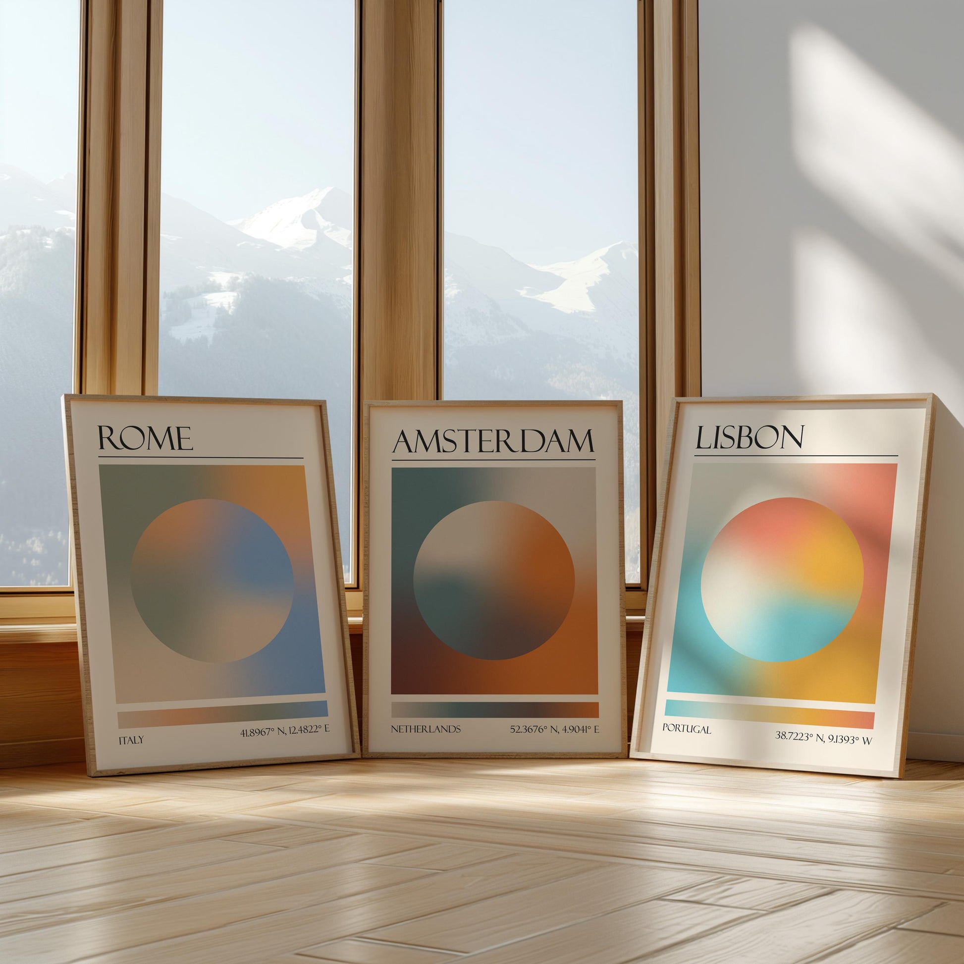 Three framed art prints with abstract designs and gradient colour palettes. The set of three triptych prints each display a city name: Rome, Amsterdam, and Lisbon. The prints are in neutral-toned wooden frames, leaning against a window.