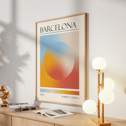 A framed print with the word "BARCELONA" at the top. The destination artwork features a colourful aura circle in teal, orange, and red. A gold lamp with four white globe lights is to the right in the hallway.