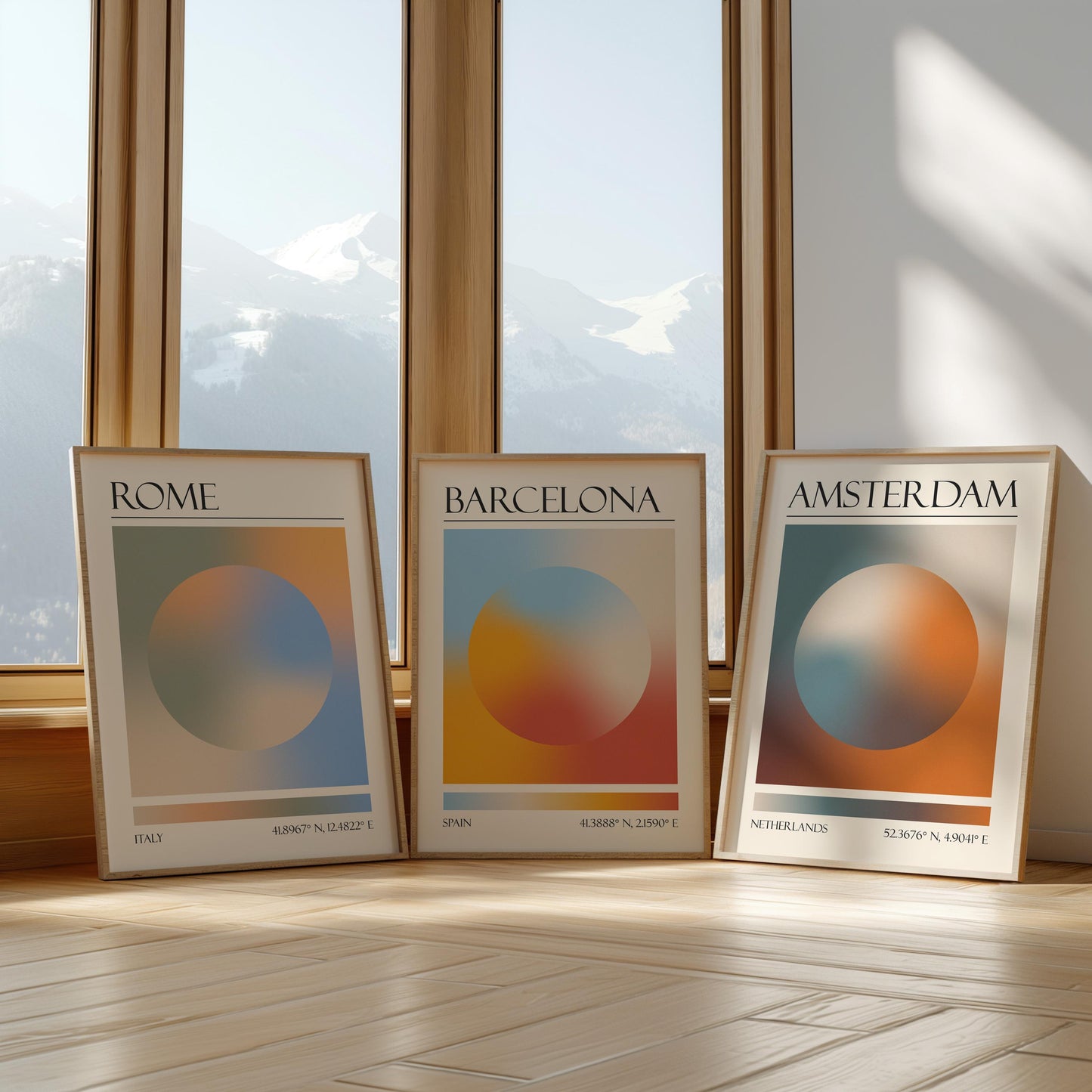 Three framed art prints with abstract designs and gradient colour palettes. The set of three triptych prints each display a city name: Rome, Amsterdam, and Barcelona. The prints are in neutral-toned wooden frames, leaning against a window.