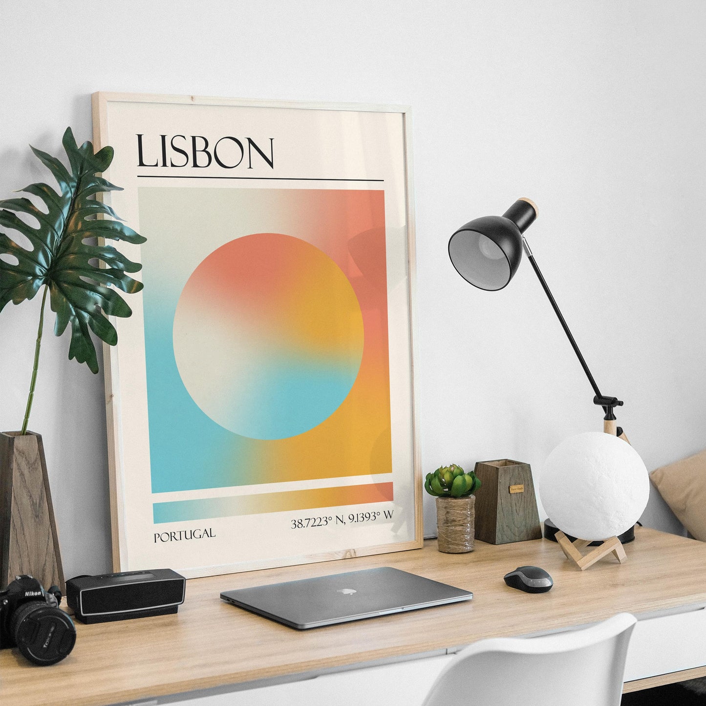 An abstract print is on a wooden desk, with a black desk lamp and a moon-shaped light in a masculine home office. The art gives a zen modern aesthetic.