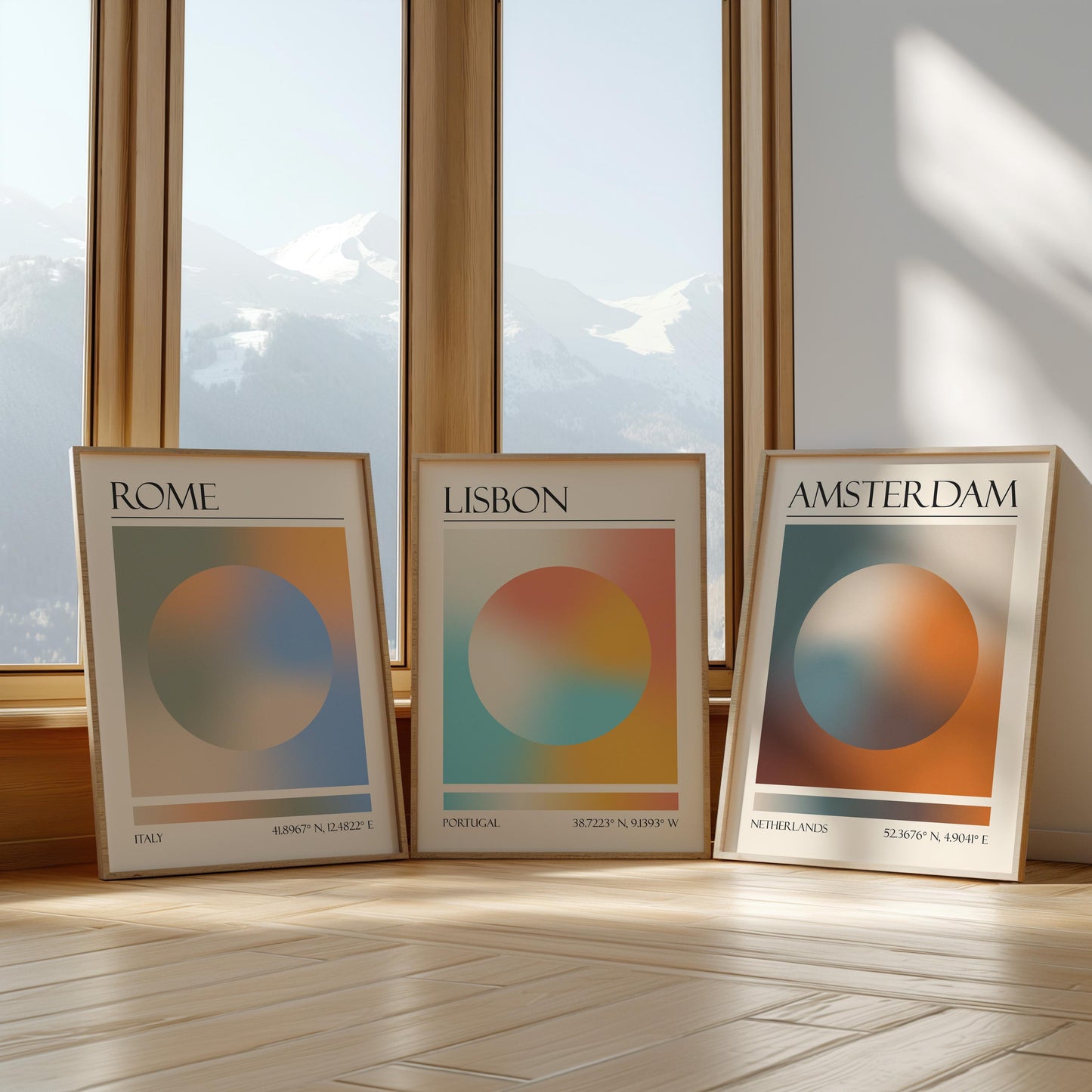 Three framed art prints with abstract designs and gradient colour palettes. The set of three triptych prints each display a city name: Rome, Amsterdam, and Lisbon. The prints are in neutral-toned wooden frames, leaning against a window.