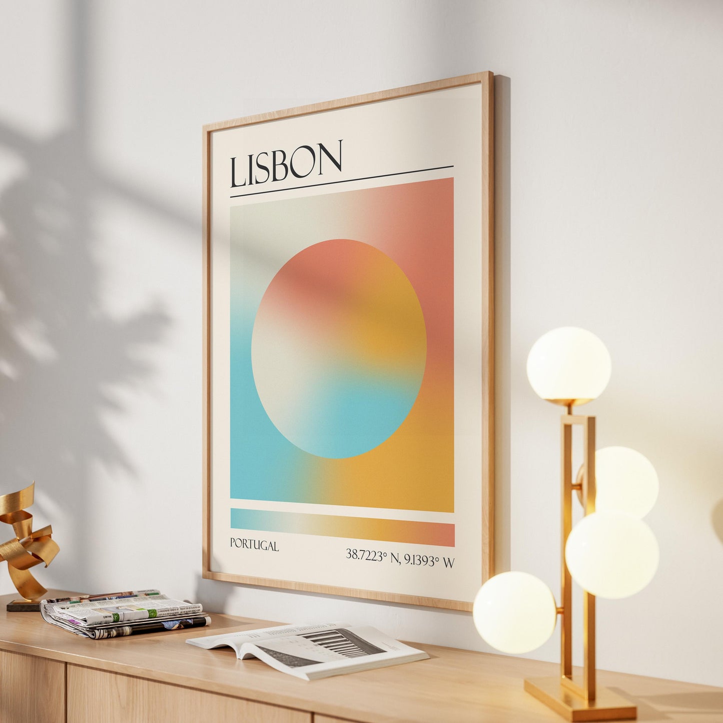 A framed print with the word "LISBON" at the top. The destination artwork features a colourful aura circle in teal, orange, and pink. A gold lamp with four white globe lights is to the right in the hallway.