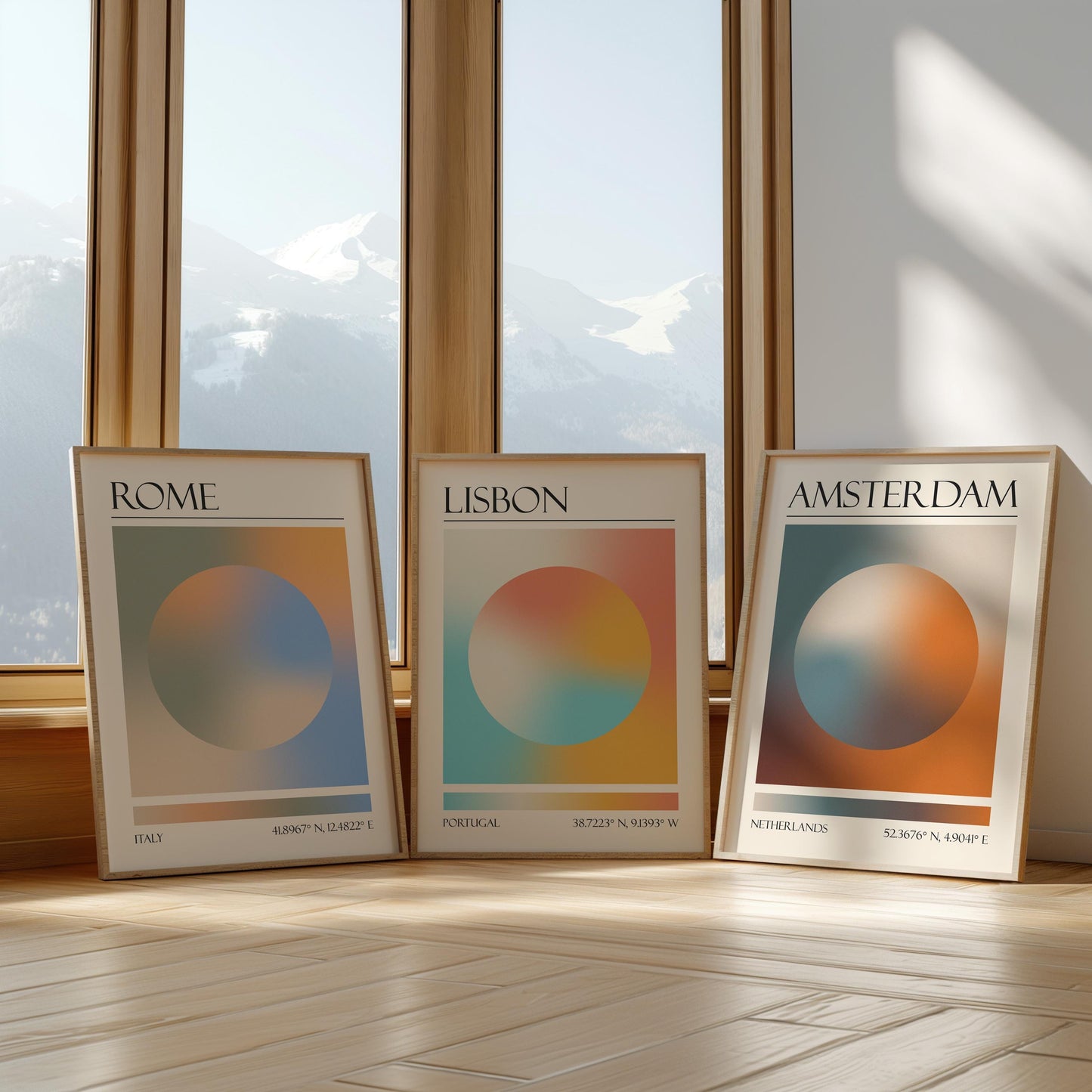 Three framed art prints with abstract designs and gradient colour palettes. The set of three triptych prints each display a city name: Rome, Amsterdam, and Lisbon. The prints are in neutral-toned wooden frames, leaning against a window.