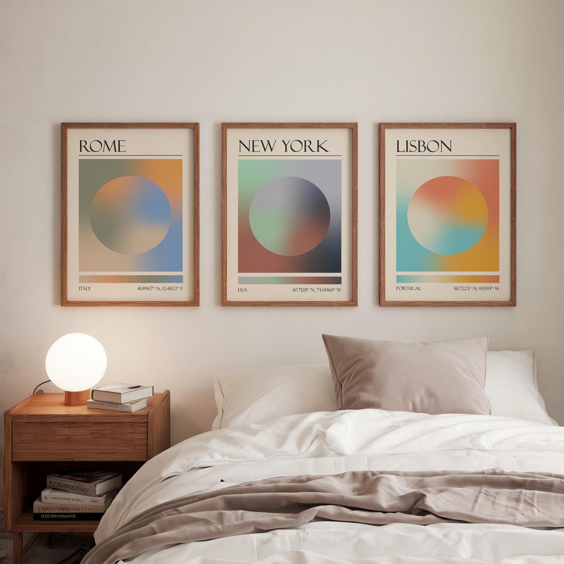 Three framed art prints, each displaying a city name: Rome, Lisbon and New York. The gallery wall prints showcase a gradient aura design in various colours. They are hung in a bedroom, with a wooden bedside table and a lamp.