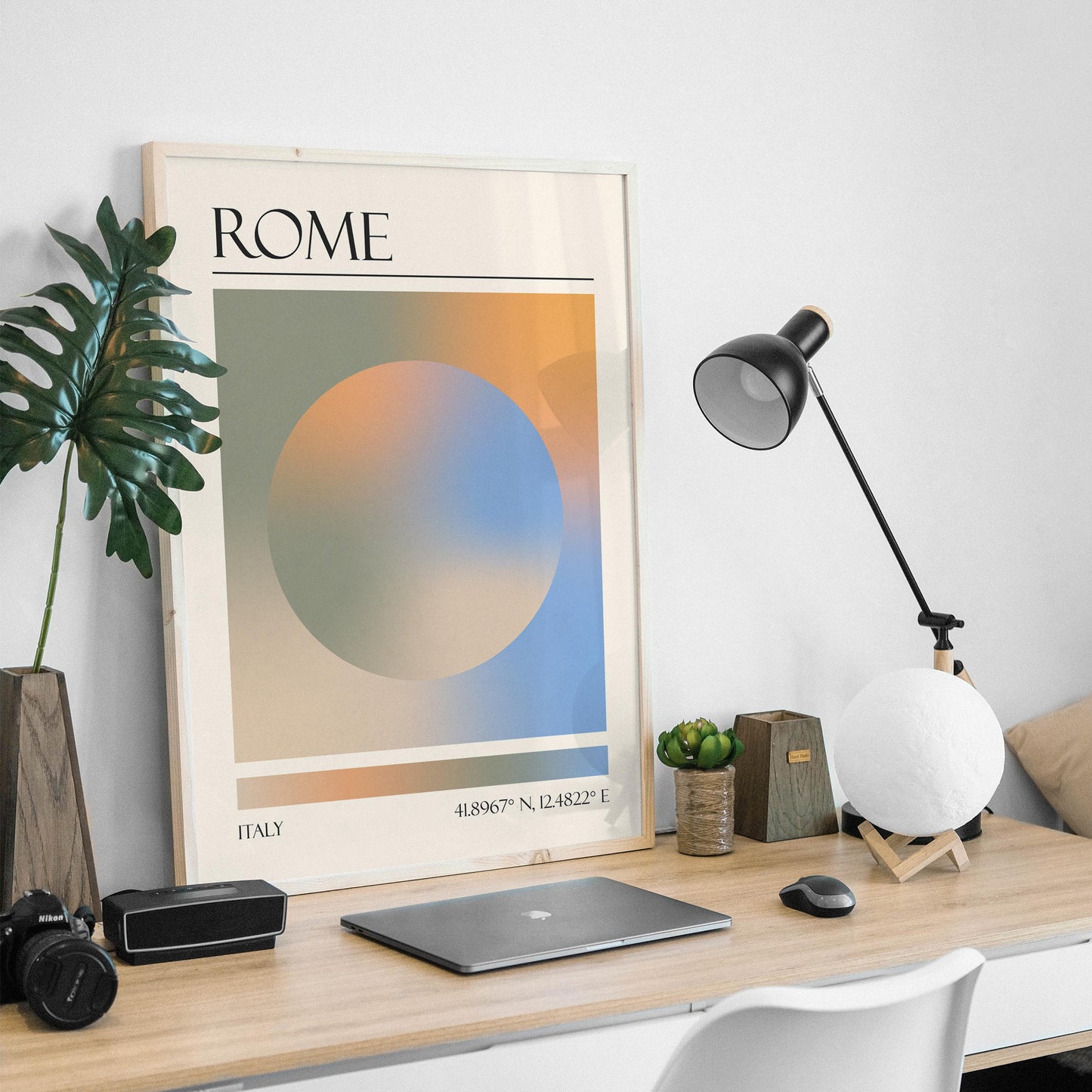 An abstract print is on a wooden desk, with a black desk lamp and a moon-shaped light in a masculine home office. The art gives a zen modern aesthetic.