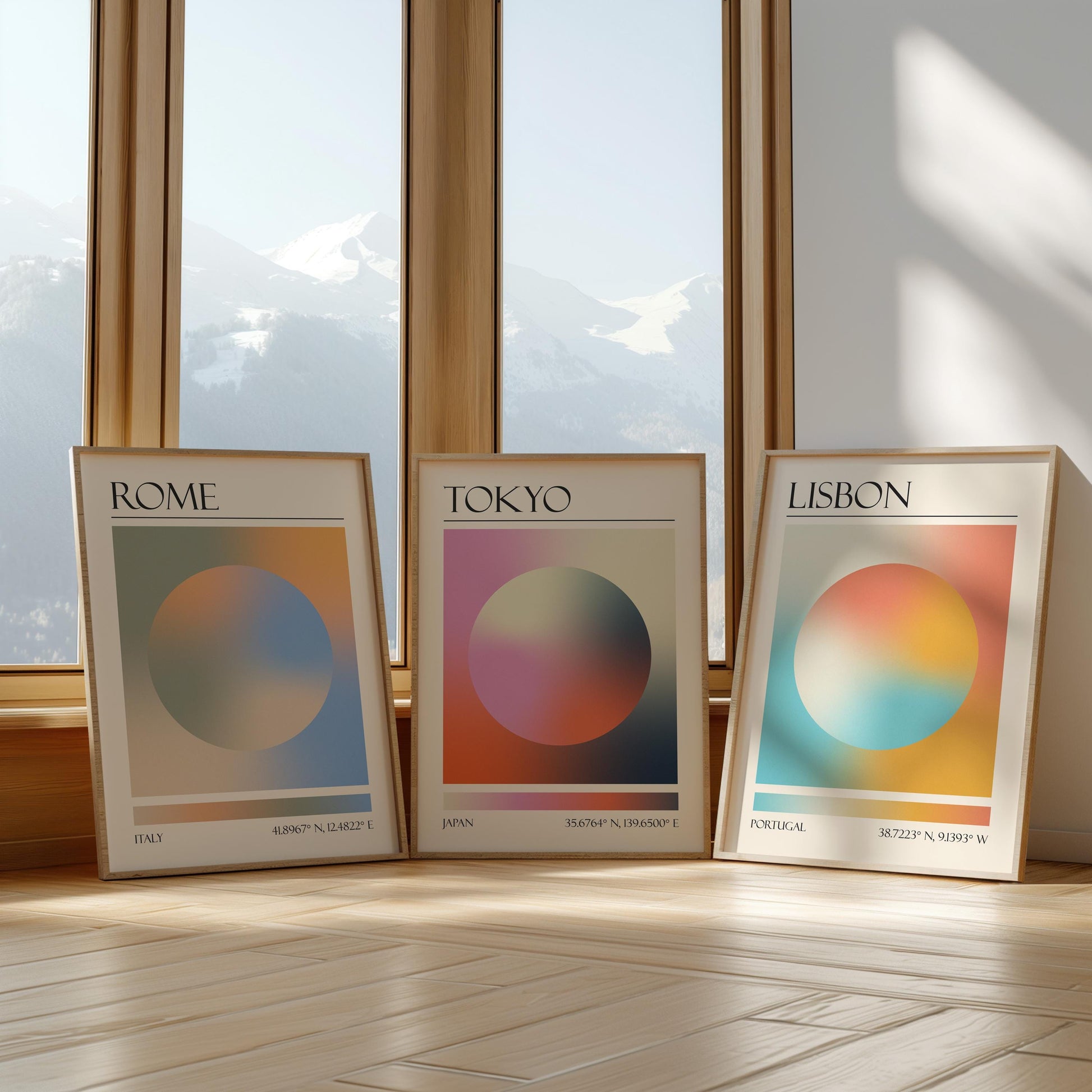 Three framed art prints with abstract designs and gradient colour palettes. The set of three triptych prints each display a city name: Rome, Tokyo, and Lisbon. The prints are in neutral-toned wooden frames, leaning against a window.