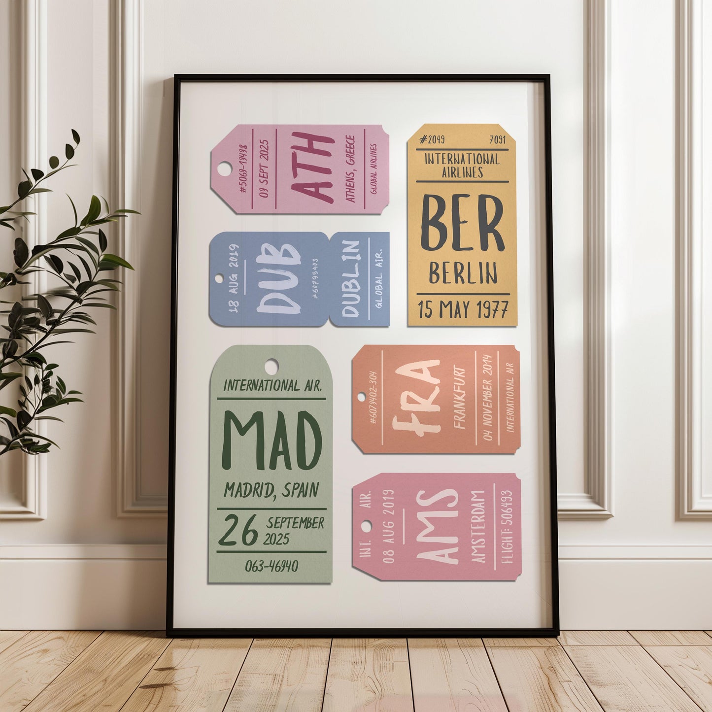 A white panelled wall and wood floor background with a black wood framed poster leaning on it. The travel lover art has personalised eclectic airport tags details and funky typography.