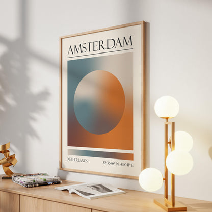 A framed print with the word "AMSTERDAM" at the top. The destination artwork features a colourful aura circle in teal, orange, and brown. A gold lamp with four white globe lights is to the right in the hallway.