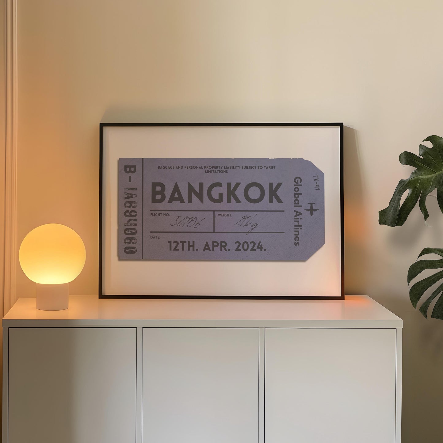 A cosy bedroom with a white chest of draws and plant. A poster is in a black frame near a lamp showing an old luggage tag design which has been made bespoke with personalised text.