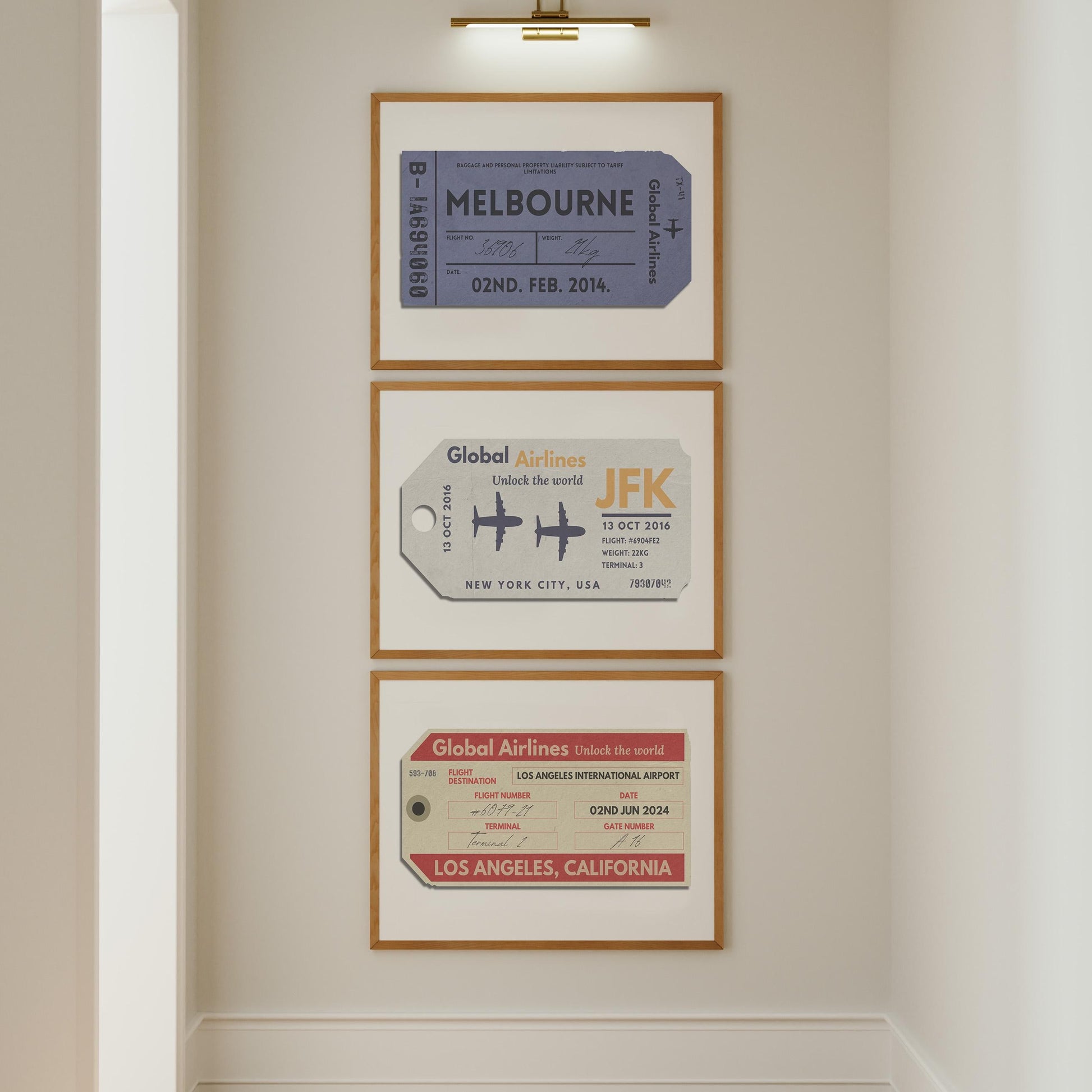 A white wall in a hallway with three posters on the wall under a gold picture lamp. The art is beige, red and blue vintage luggage tags in landscape frames.