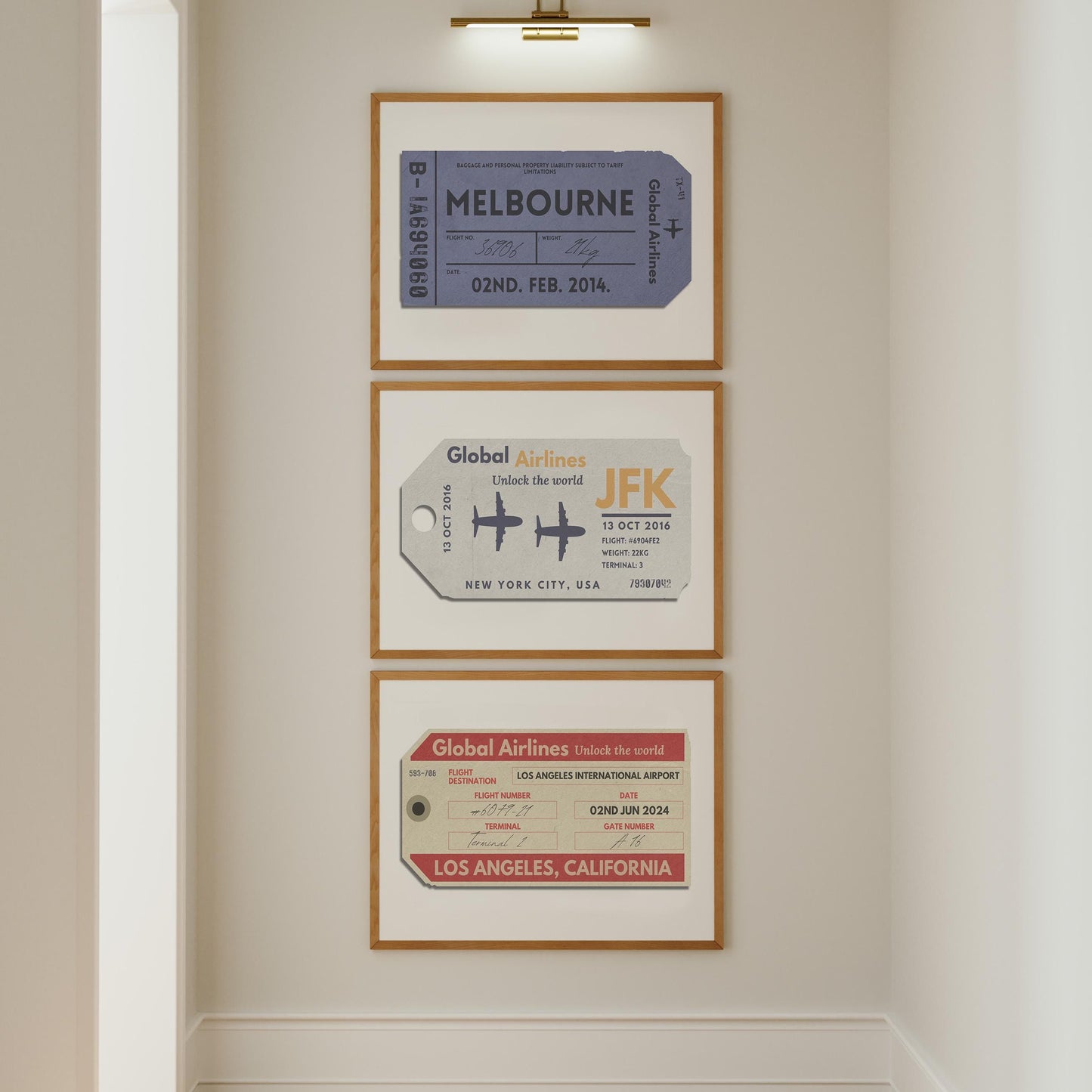 A white wall in a hallway with three posters on the wall under a gold picture lamp. The art is beige, red and blue vintage luggage tags in landscape frames.
