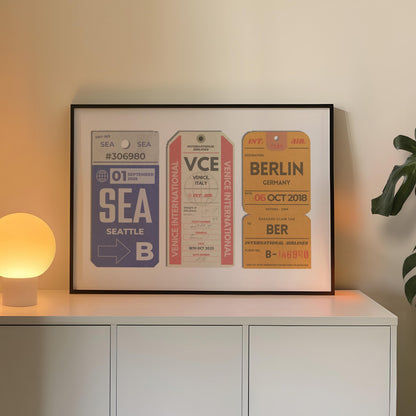A cosy bedroom with a white chest of draws and plant. A poster is in a black frame near a lamp showing three old luggage tag designs which has been made bespoke with personalised text.