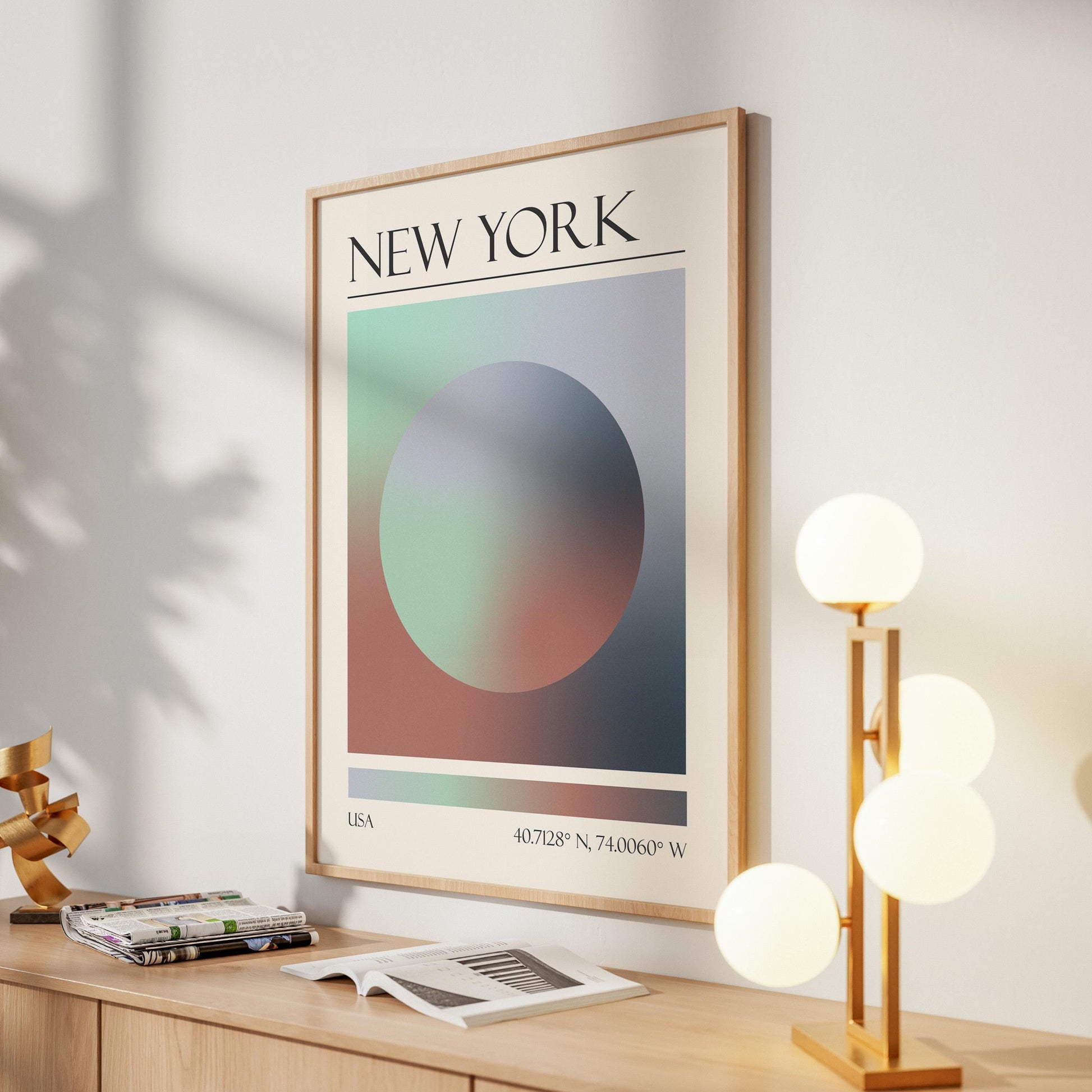 A framed print with the word "NEW YORK" at the top. The destination artwork features a colourful aura circle in teal, grey, and pink. A gold lamp with four white globe lights is to the right in the hallway.