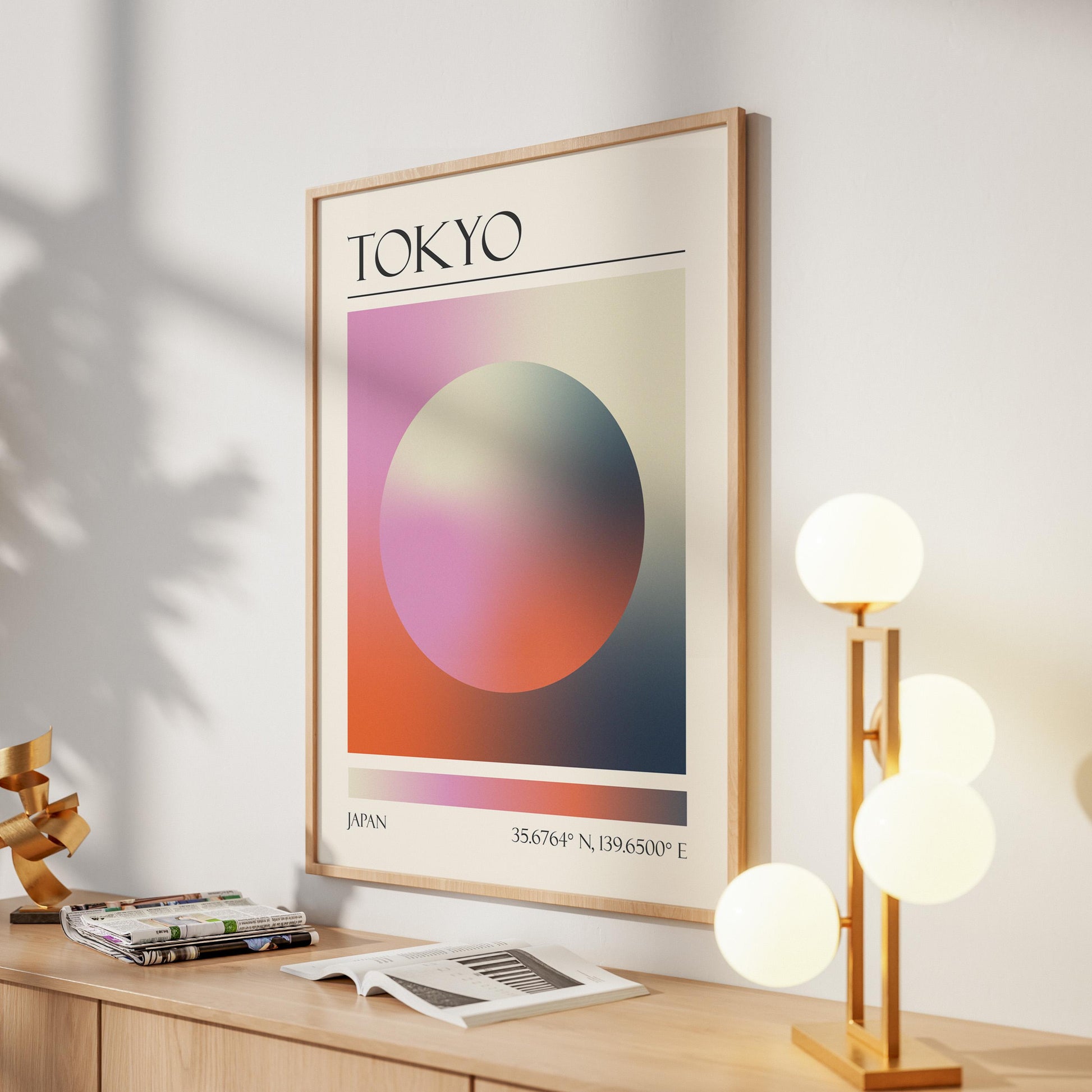 A framed print with the word "TOKYO" at the top. The destination artwork features a colourful aura circle in pink, orange and black. A gold lamp with four white globe lights is to the right in the hallway.