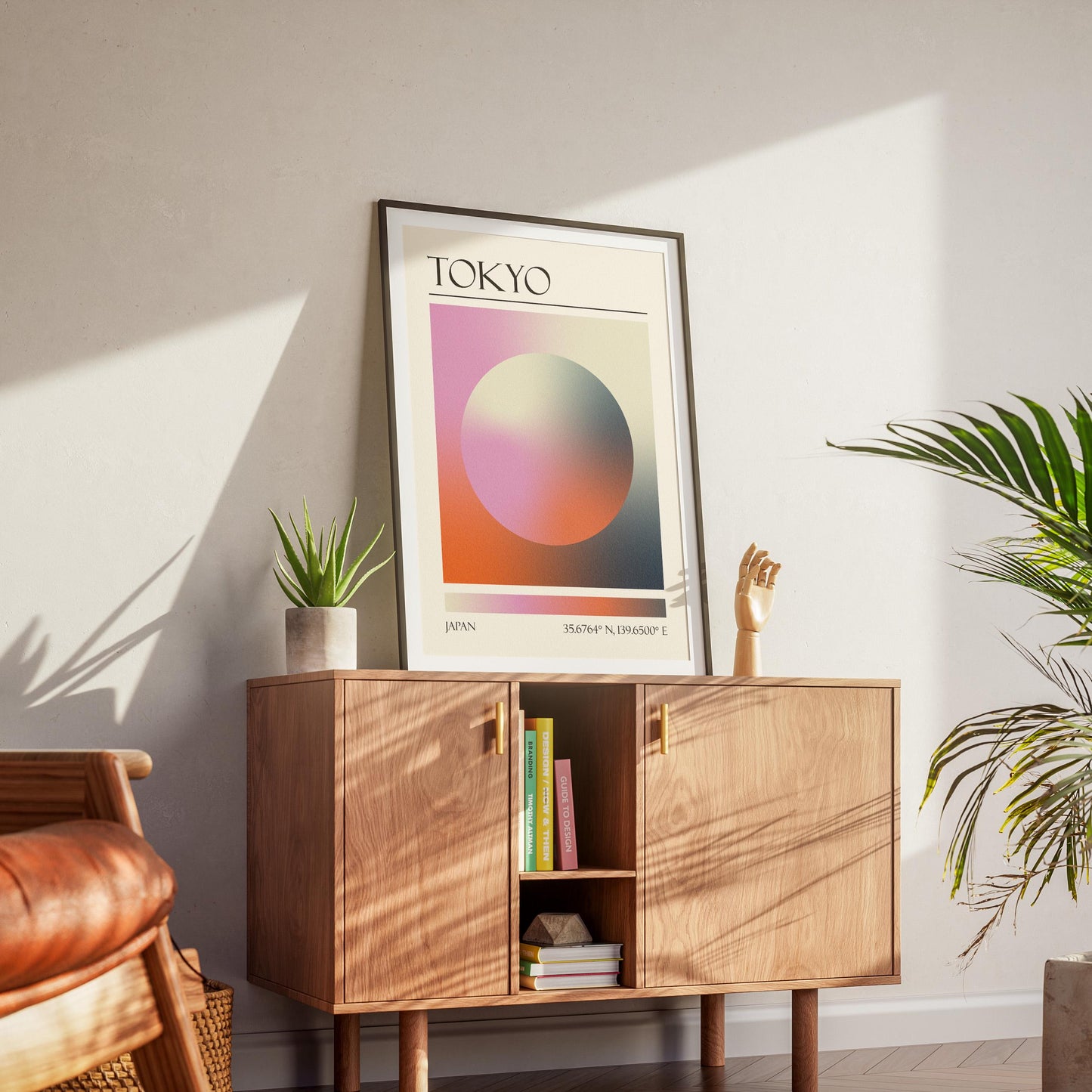 A black frame with an aura gradient circle print inside. The word "TOKYO" and coordinates are at the bottom. The memory keepsake print is displayed on a wooden cabinet with gold handles.