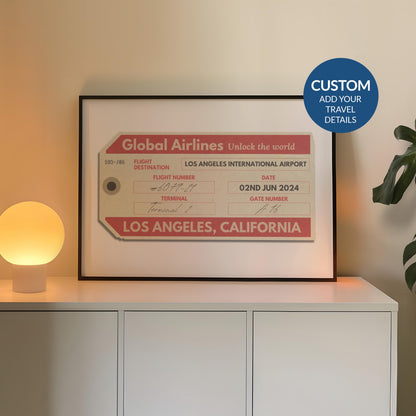 A cosy bedroom with a white chest of draws and plant. A poster is in a black frame near a lamp showing an old luggage tag design which has been made bespoke with personalised text.