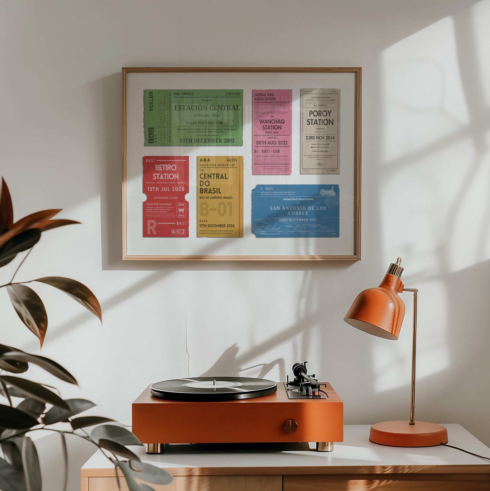 A orange lamp and vinyl player on a counter. A horizontal print is hung above which displays a nostalgic personalised eurail ticket stub poster in bright colours wth rustic aged details.