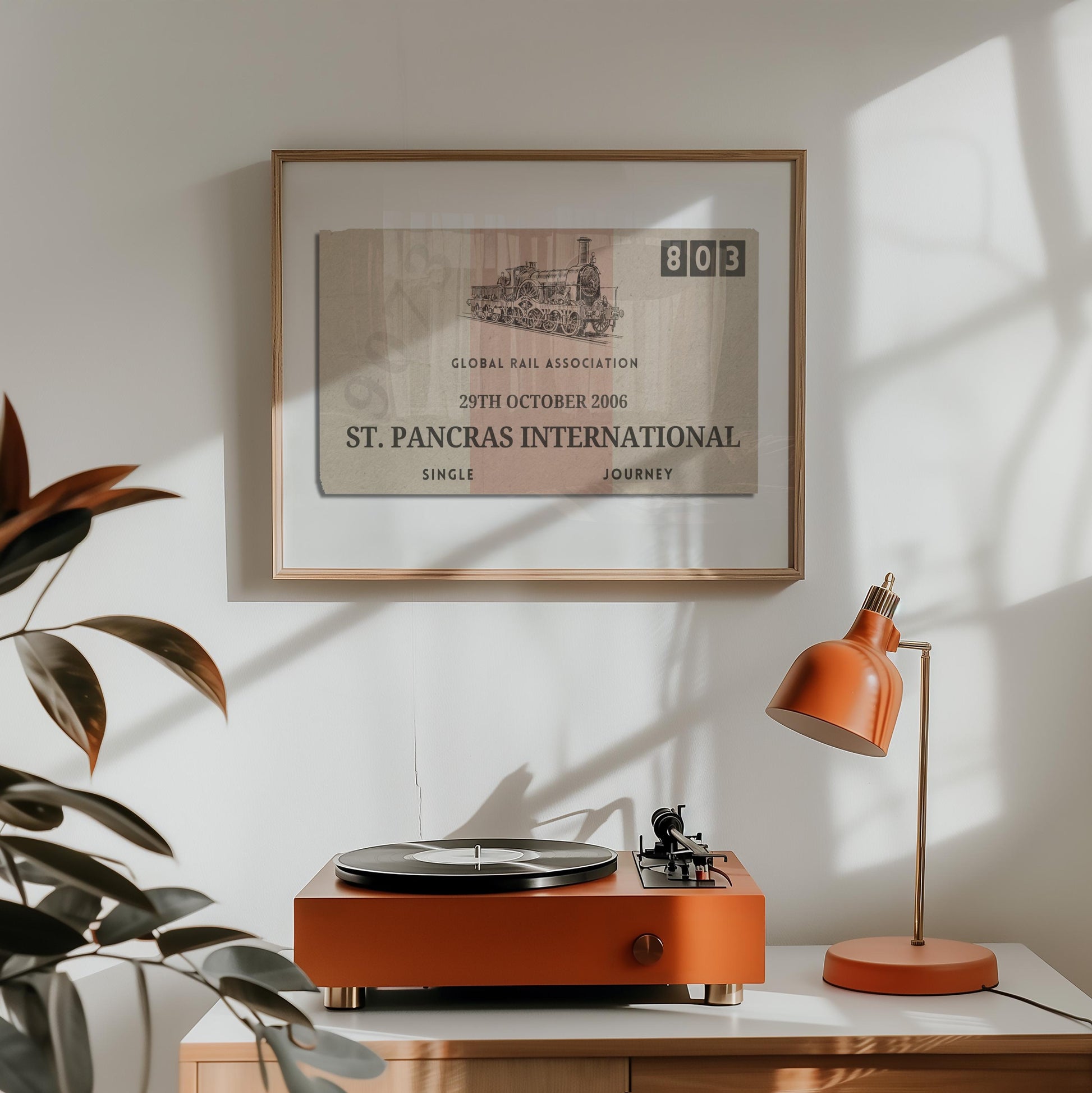 A orange lamp and vinyl player on a counter. A horizontal print is hung above which displays a nostalgic personalised eurail ticket stub poster in a rustic cream colour with rustic aged details.