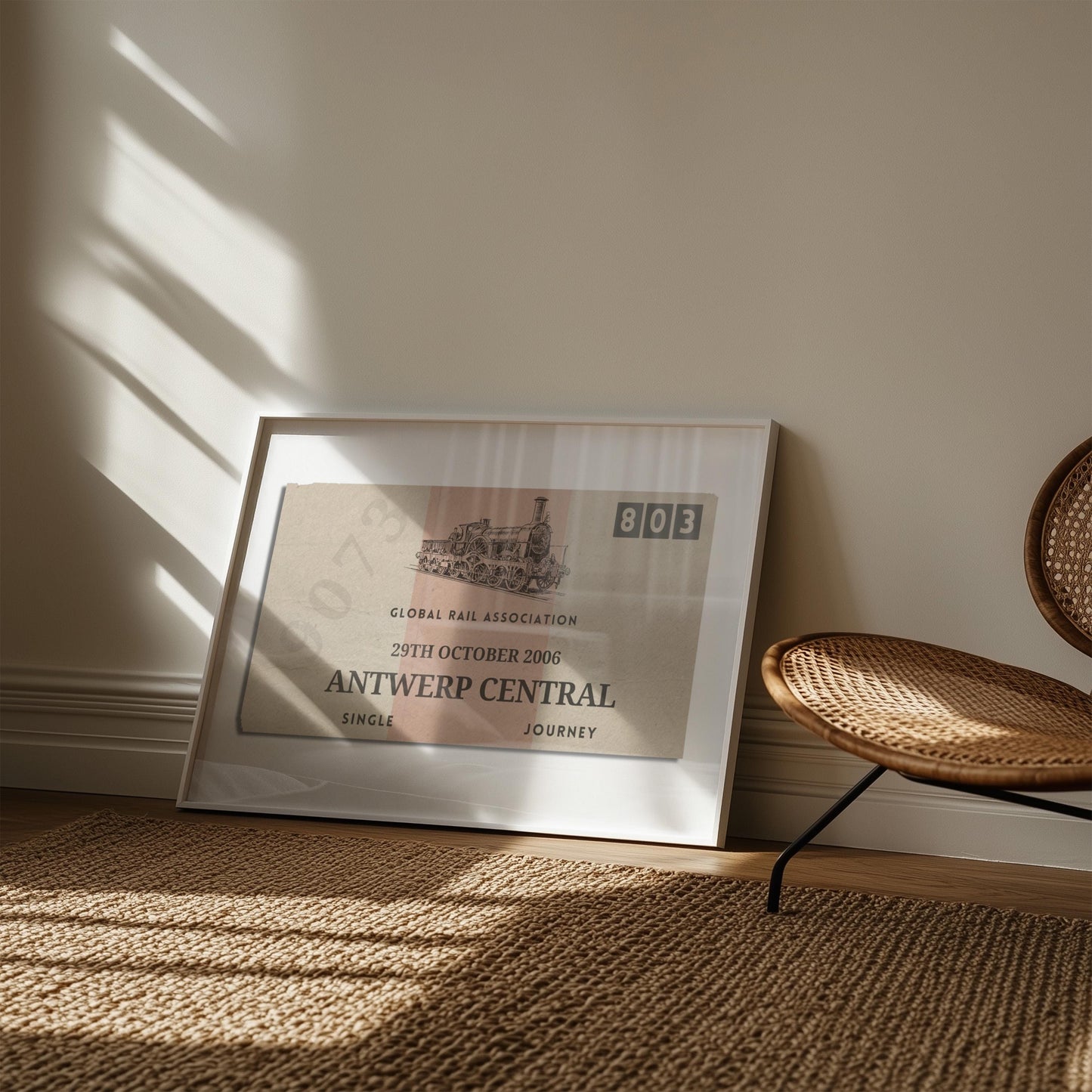 A muted tone of colour art print showing a retro railway tag with custom details on them. The art is leaning on the wall in a boho style living room with a rattan rug and chair.