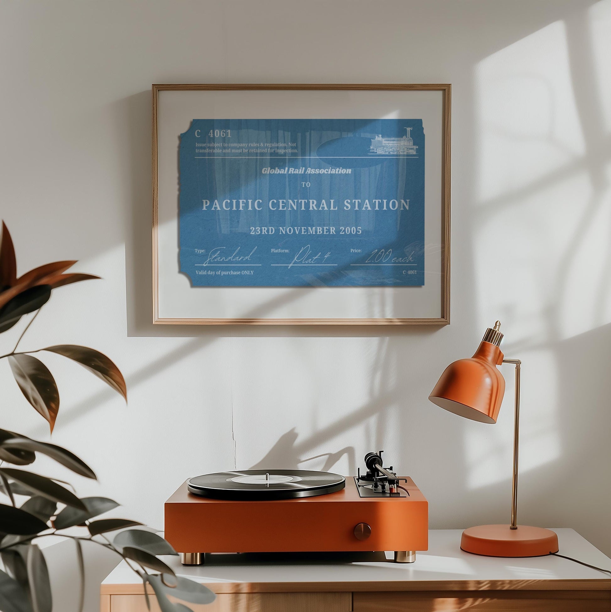A orange lamp and vinyl player on a counter. A horizontal print is hung above which displays a nostalgic personalised eurail ticket stub poster in a rustic blue colour with rustic aged details.