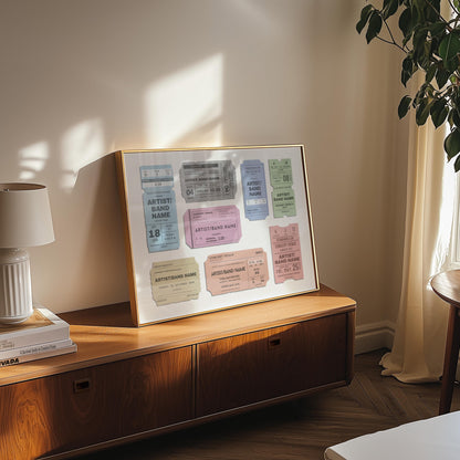 A cosy bedroom with a wood draw unit and a lamp above. Art is leaning on the wall which has colourful festival ticket passes on it with bespoke text. It is a custom made music lover design.