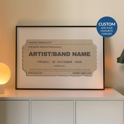 A cream coloured concert ticket design on a poster in a black frame in a warm lit office space. The art is personalised and has custom text details.