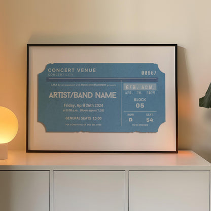 A blue coloured concert ticket design on a poster in a black frame in a warm lit office space. The art is personalised and has custom text details.