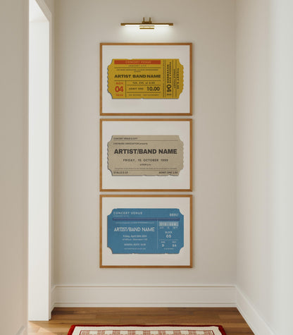 A white hallway with a set of three tryptich home decor prints on the wall under a gallery light. A yellow, blue and beige concert ticket stub is on each with bespoke artist names and details from past events.