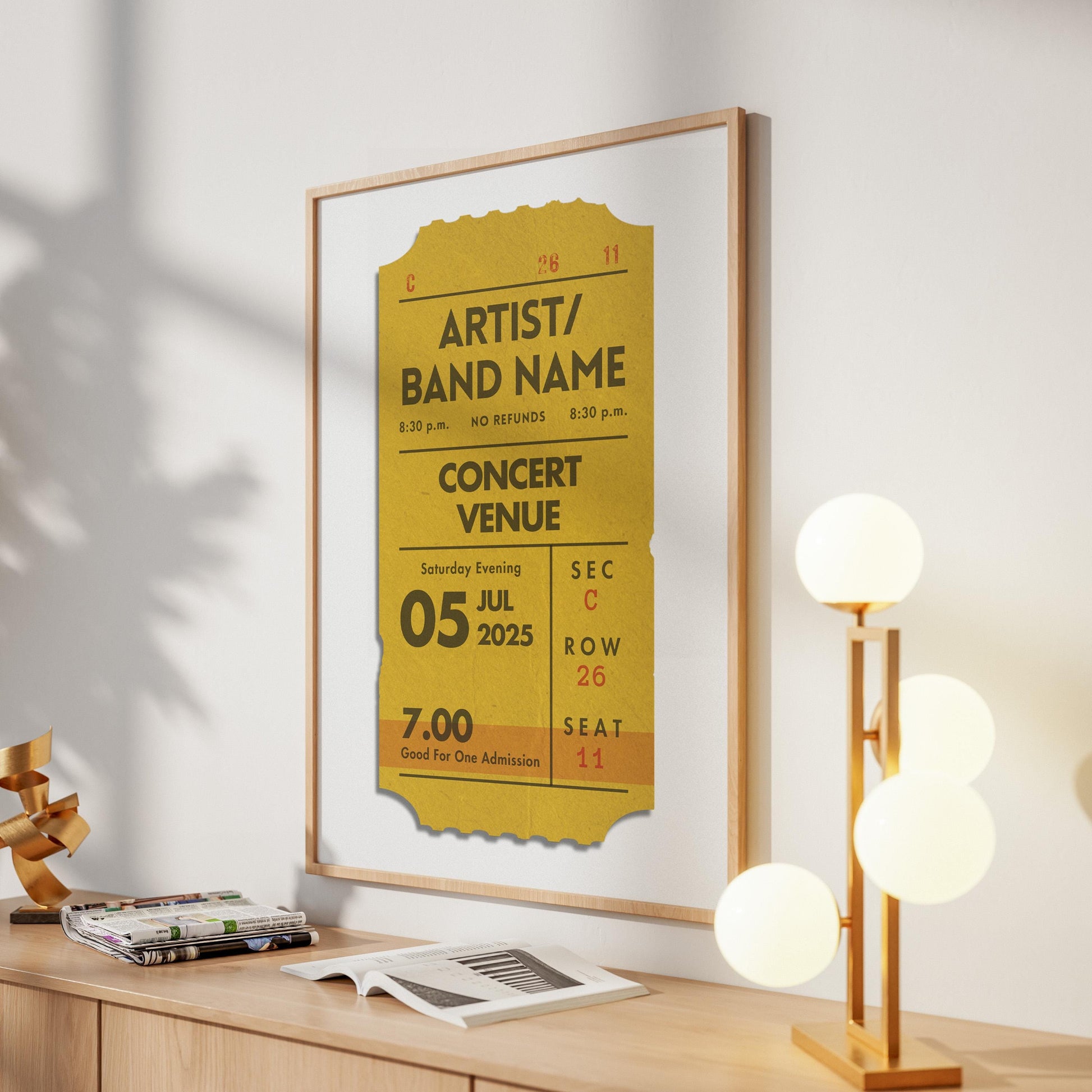 A yellow coloured concert ticket design on a poster in a wood frame in a warm lit hallway space. The art is personalised and has custom text details.