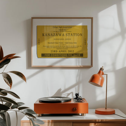 A orange lamp and vinyl player on a counter. A horizontal print is hung above which displays a nostalgic personalised eurail ticket stub poster in a rustic yellow colour with rustic aged details.