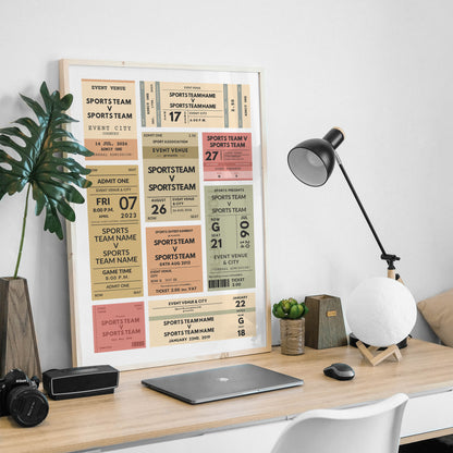 A framed sports team ticket-style wall art print hangs on a light wood desk in a styled home office. The print features multiple vintage inspired ticket designs in cream, tan, coral, and muted red.