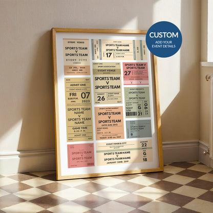 A framed sports ticket wall art print leaning against a wall in a room with a checkered floor. The print features multiple colorful event tickets with customizable text and a blue circular badge that reads 'CUSTOM ADD YOUR EVENT DETAILS'.